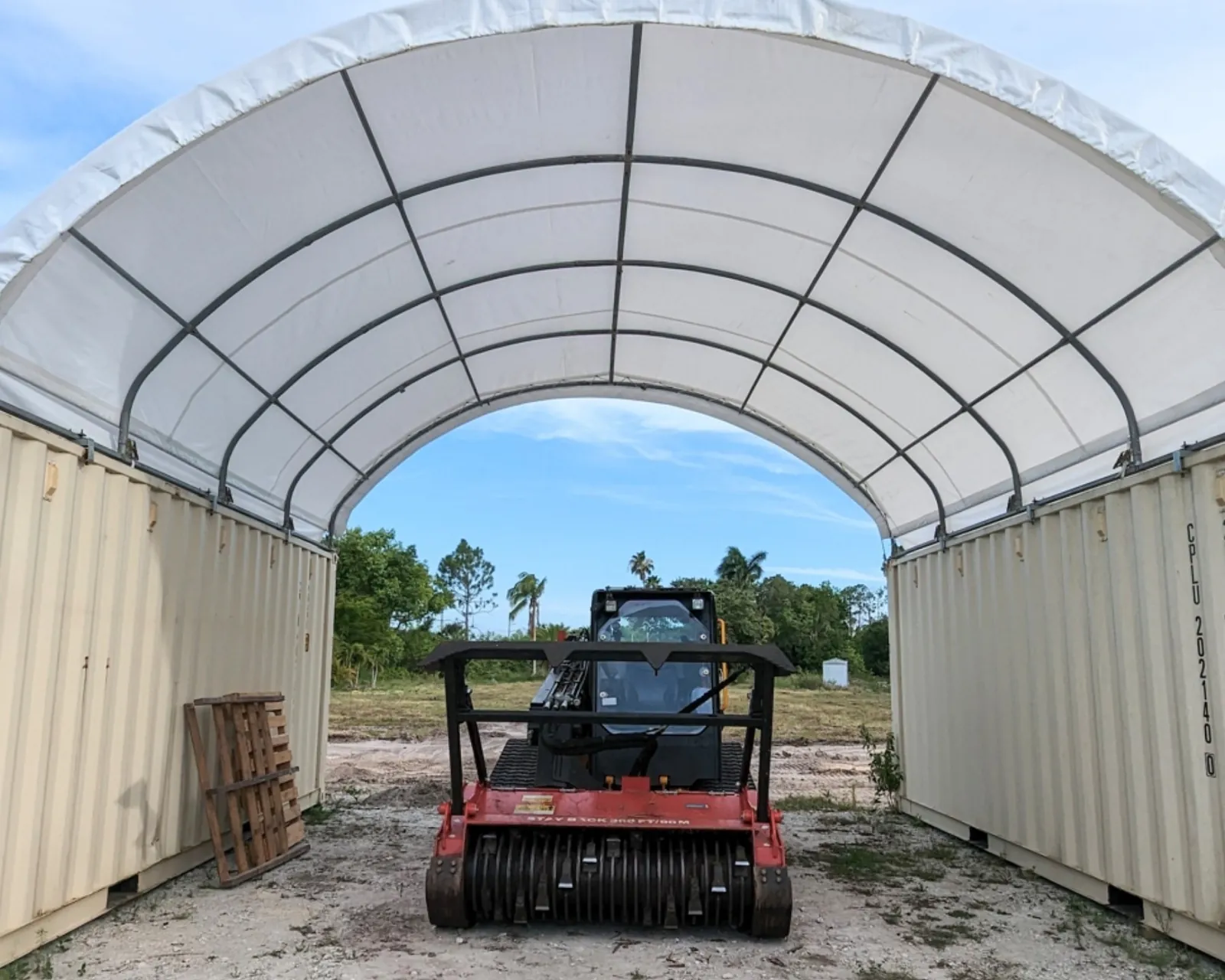 Covermore container shelter over two shipping containers at a customer's site in Florida, with a skid steer parked under the arch